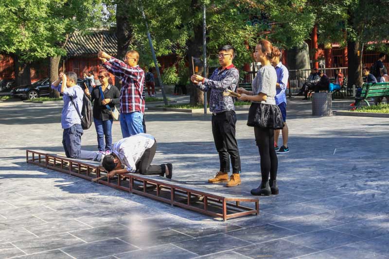 Chinese young people praying with incense in front of Yonghegong Lama Temple in Beijing, China