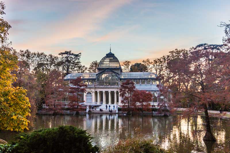 Crystal Palace, behind artificial lake with trees and winter sky in Retiro park, Madrid