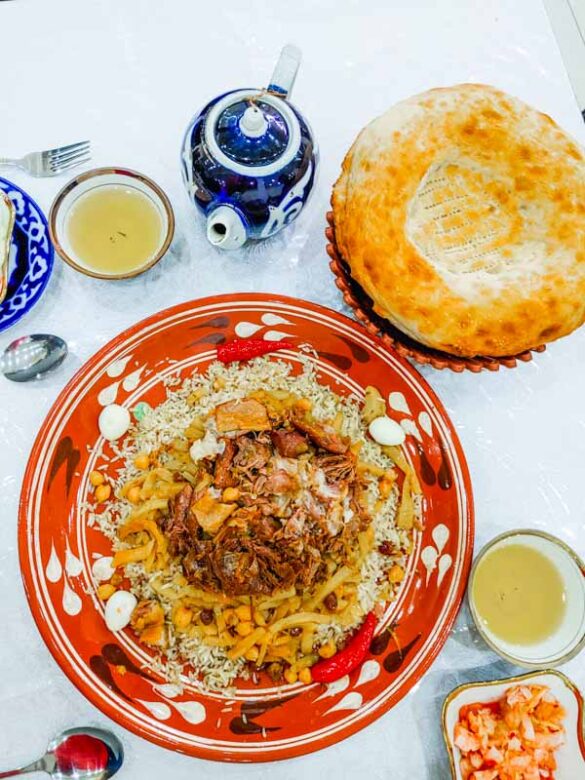 Gran plato de plov en Samarcanda, plato nacional de Uzbekistán, con té verde, ensaladas y pan