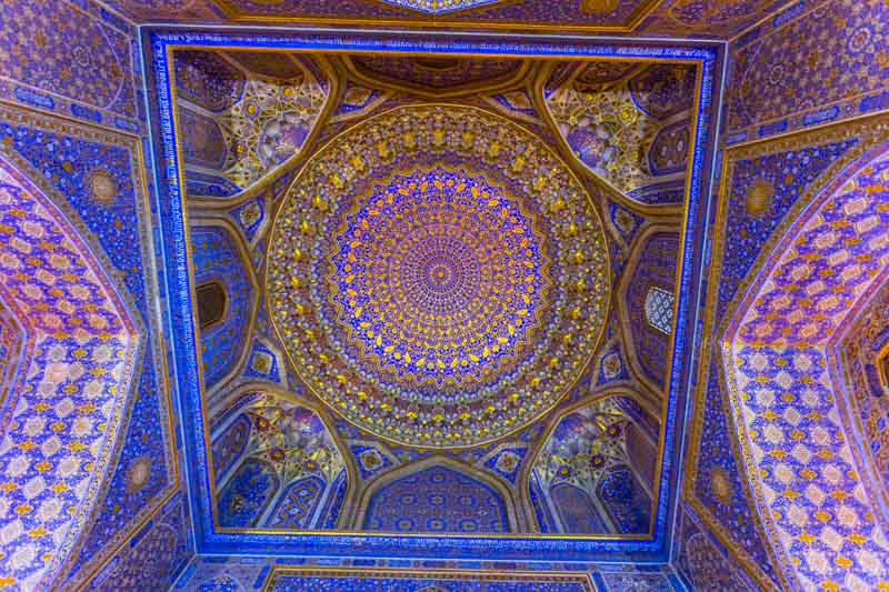 Monumental cúpula decorada con oro y azul de la Madrasa Tilya-Kori, en el Registan de Samarcanda, con forma de cuadrado y círculo.